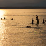Silhouette Of Young People Playing In The Sea In Sunset