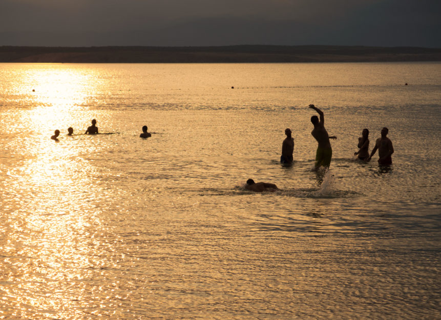 Silhouette Of Young People Playing In The Sea In Sunset