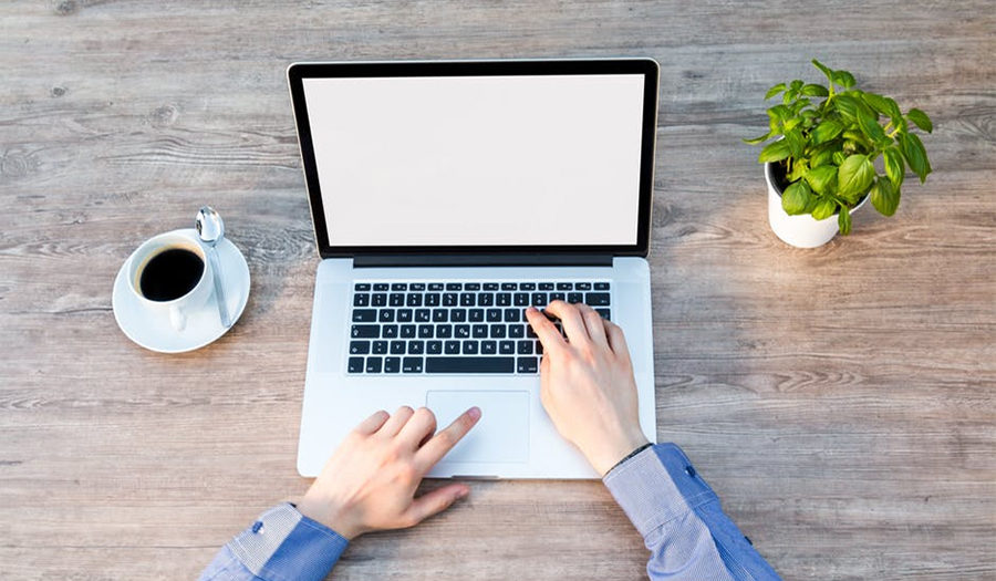 Web designer working on laptop. On the desk is also coffee and small flower.