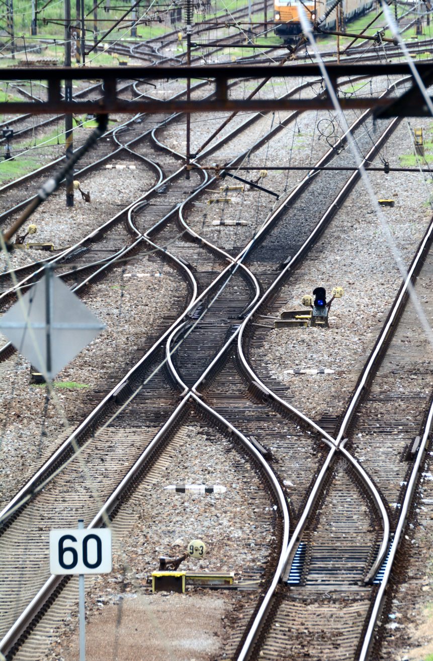 Train railway tracks. Vertical photo of train tracks at the railway station. One track zigzags cross several other straight tracks. At the rear is a yellow locomotive that is approaching the switches.
